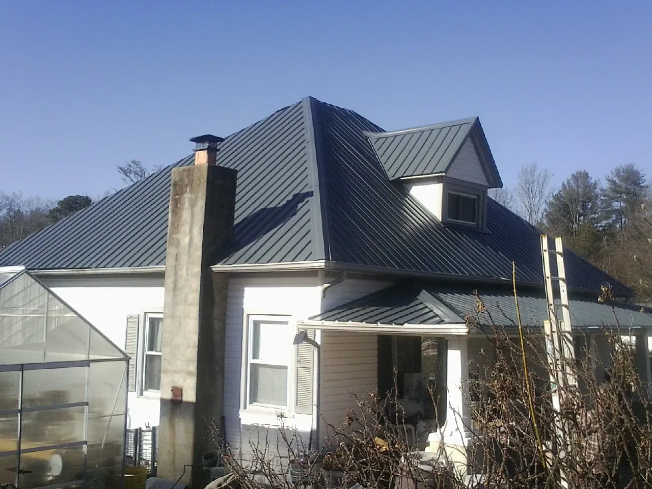 Dark blue standing seam metal roof on a white farmhouse with dormer — Slate & Tile Roof Repair by Roofing Brothers in Saint Louisville