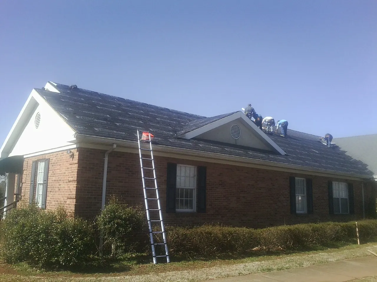 Crew tearing shingles off a brick ranch roof with a ladder set — Metal Roof Repair work by our crew in Saint Louisville