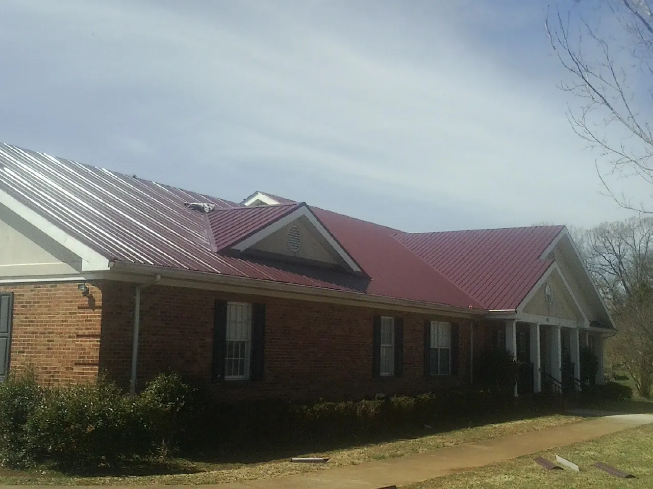 Red metal roof with gabled entries on a long brick building, from a Hail Damage Roof Repair job in Saint Louisville