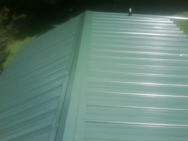 New green metal panels meeting at the ridge of a roof — Flat Roof Repair work by our crew in Saint Louisville
