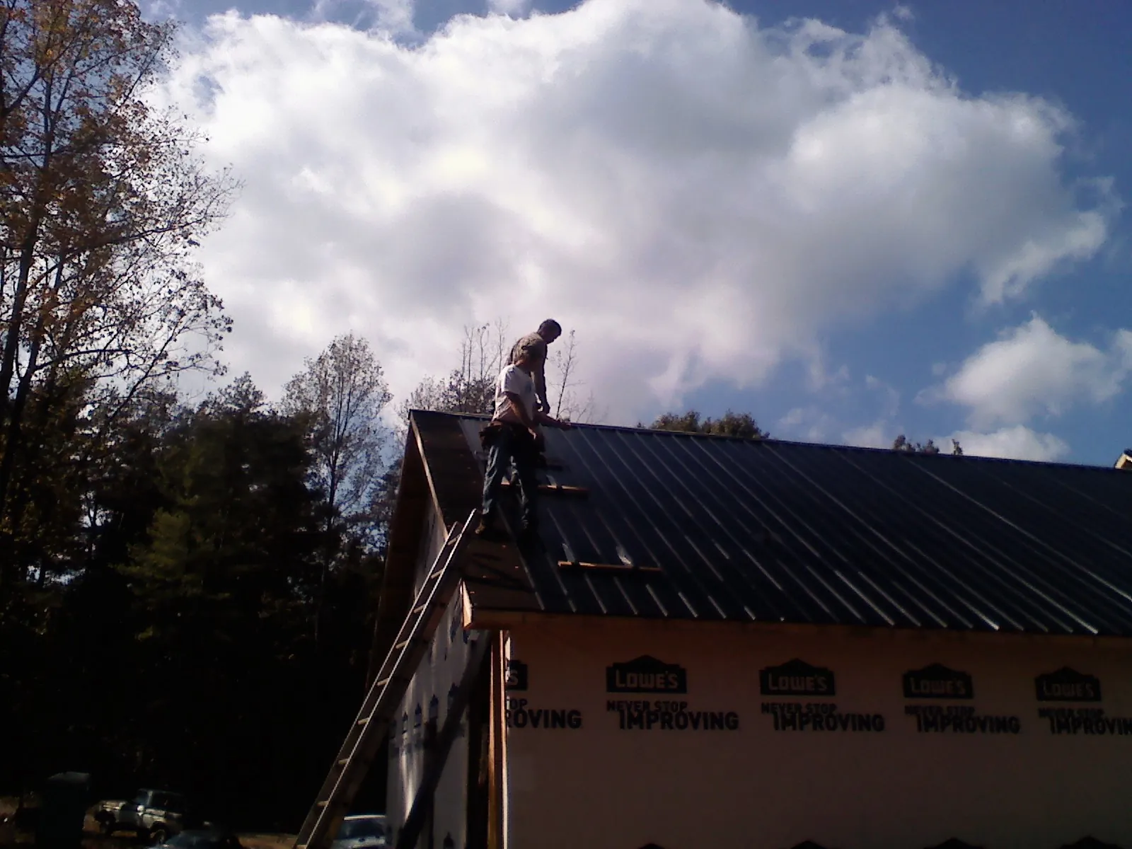 Roofer fastening dark metal panels high against a cloudy sky, from a Roof Inspection job in Saint Louisville