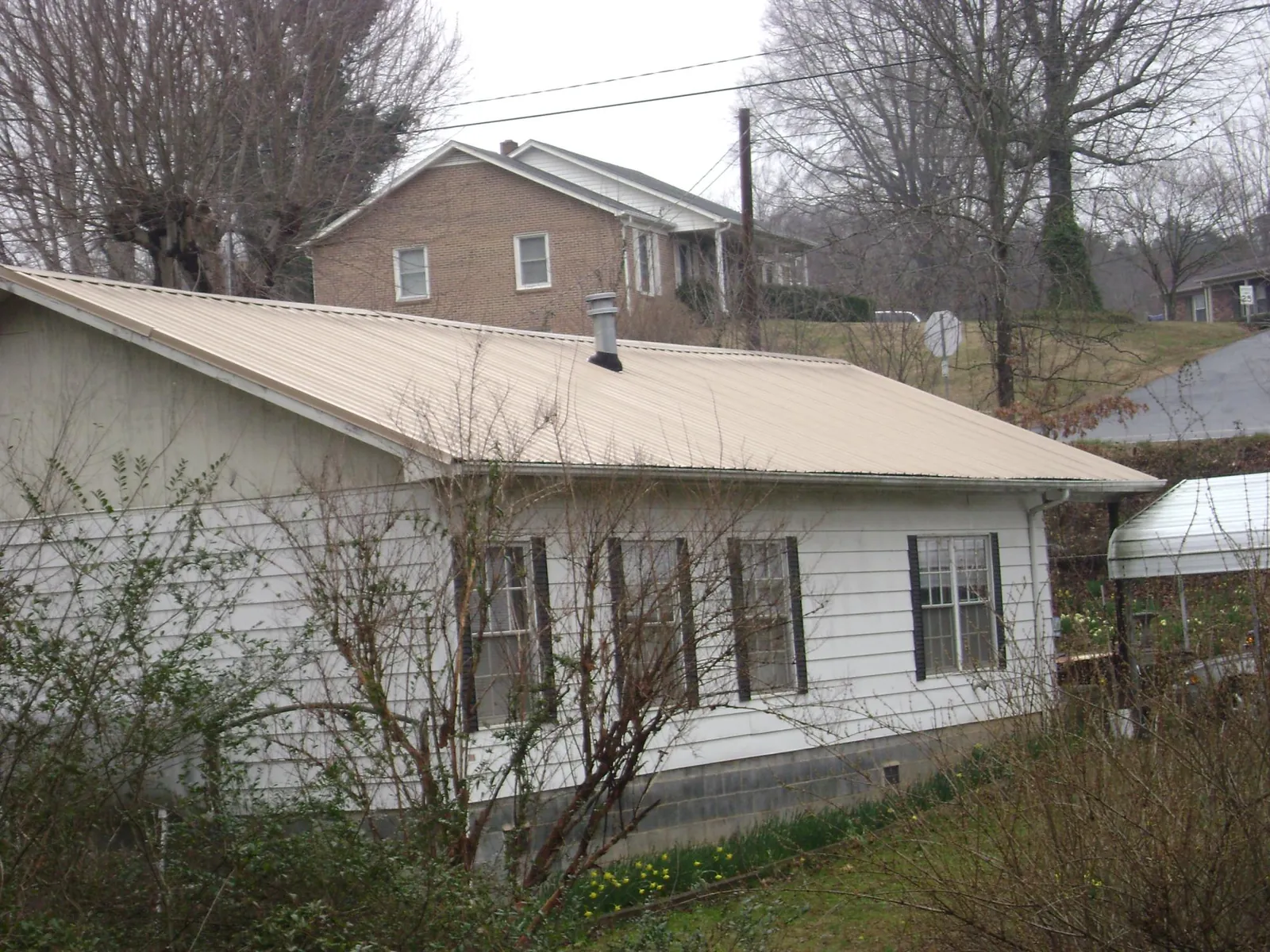 Tan metal roof on a white sided house set into a hillside — Commercial Roofing by Roofing Brothers in Saint Louisville