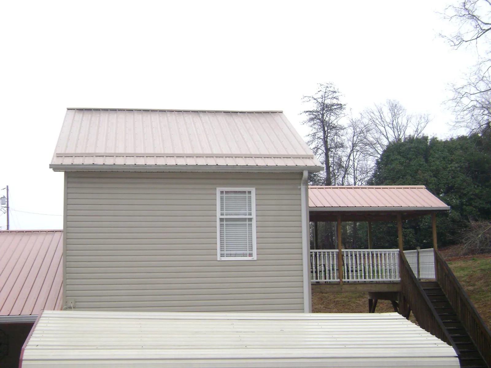 Tan metal roofs on a two story addition and attached porch, from a Roof Replacement job in Saint Louisville